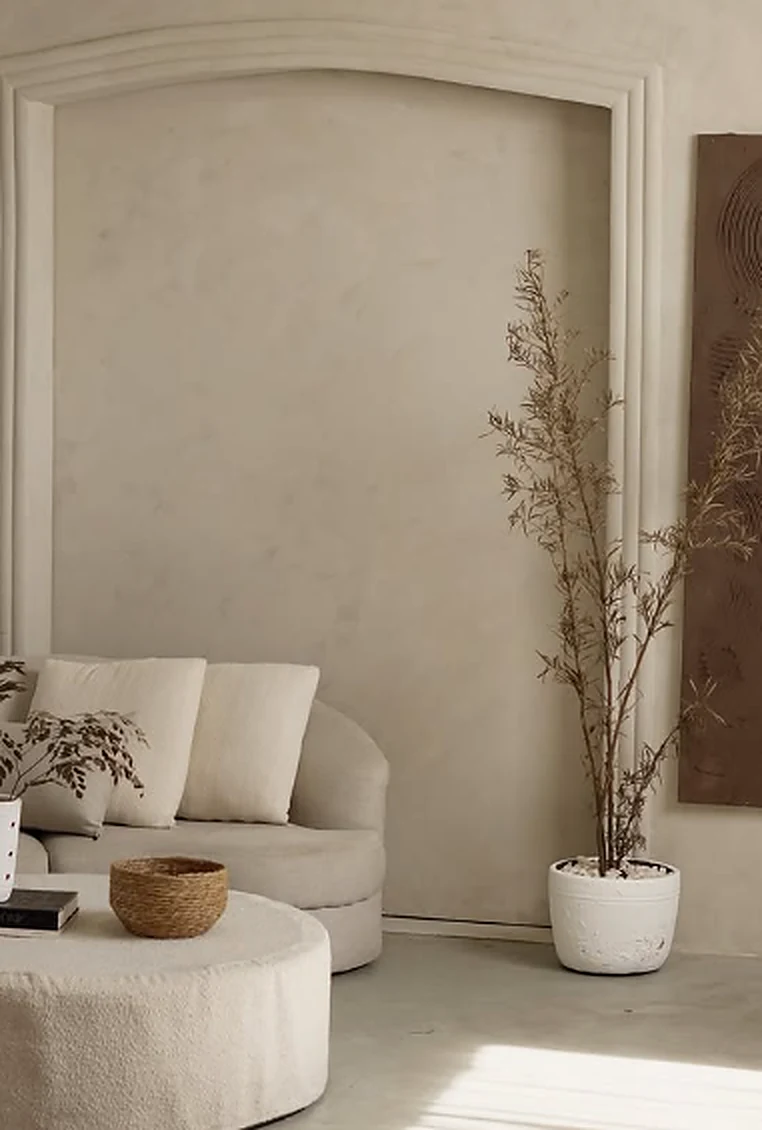 Sala do Casarão com sofá claro, mesa arredondada, arco na parede e plantas secas