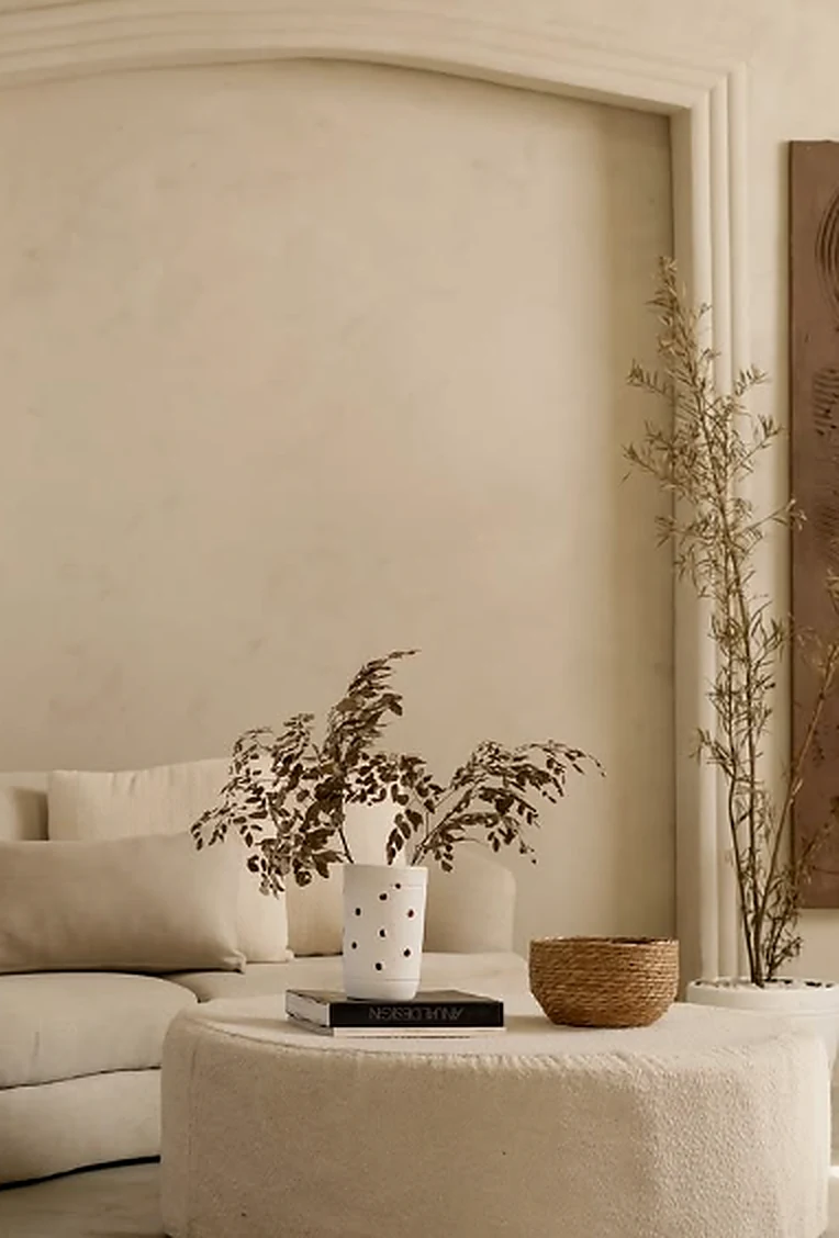 Outro enquadramento da sala clara com sofá curvo, mesa de centro e vegetação ornamental